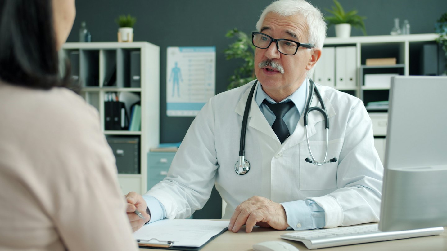 Doctor with pen discusses chart with patient at desk.