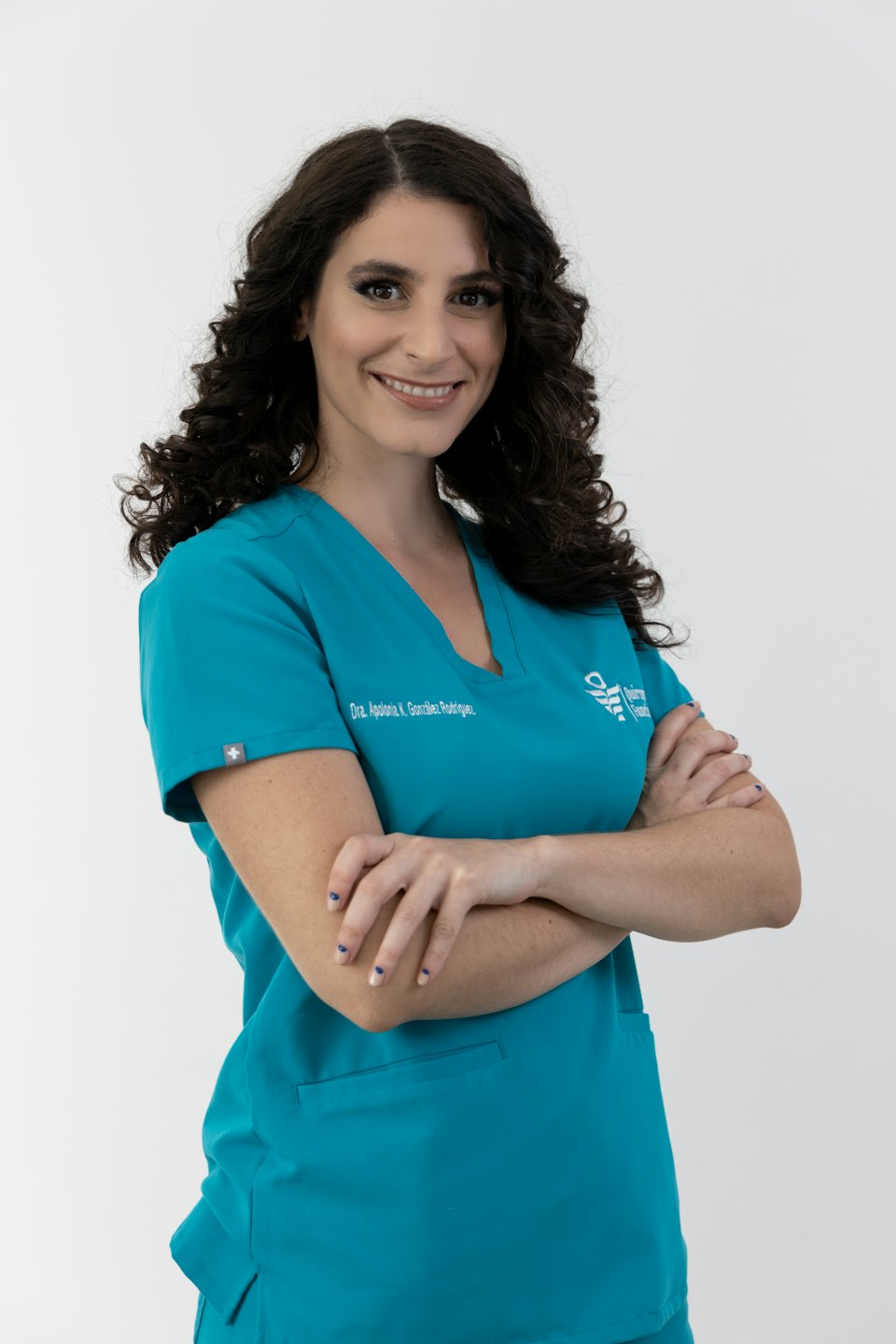 Smiling medical professional in teal scrubs standing with arms crossed.