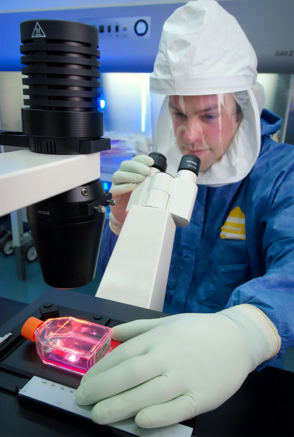 Scientist in blue suit examining sample under microscope in lab.